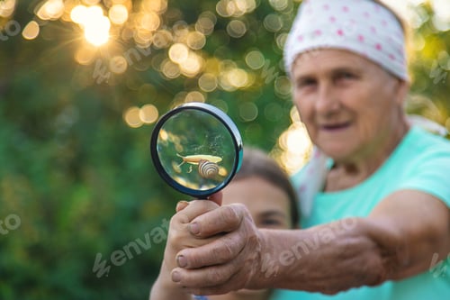 Preview: Grandmother and child are studying the snail in the park. Selective focus.