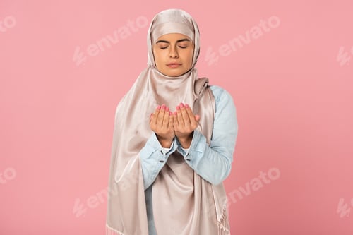 Preview: attractive muslim woman in hijab praying isolated on pink