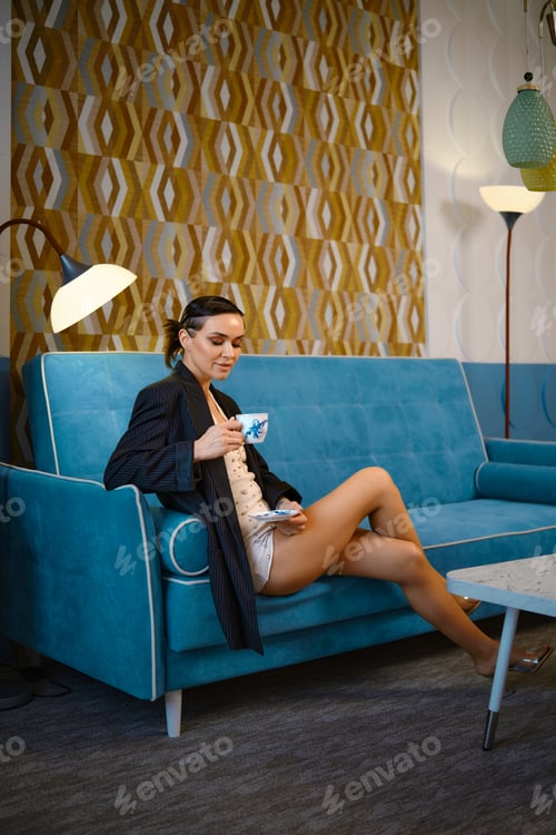Preview: Fashionable woman sitting on the sofa looking thoughtfully into a cup of tea