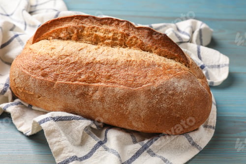 Preview: Fresh loaf of bread on light blue wooden table, closeup