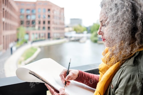 Preview: Portrait of mature woman artist making a drawing over a canal in London.