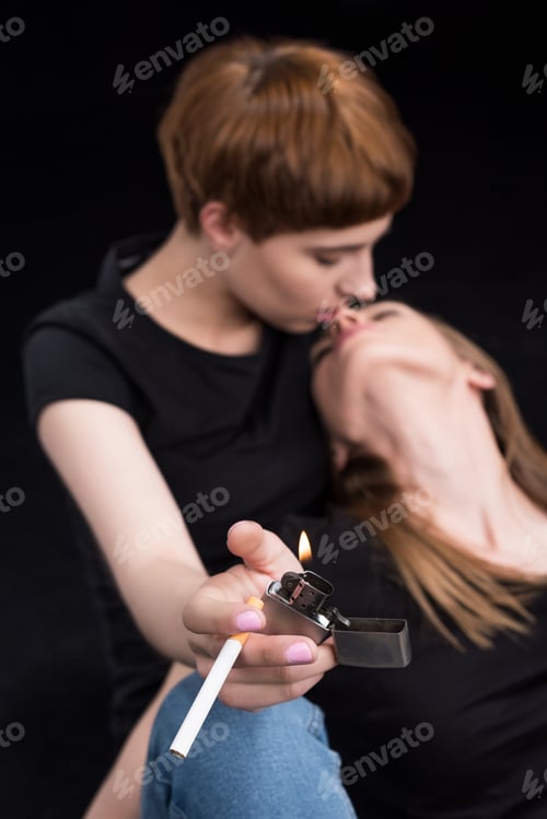 Preview: Half-length shot of young woman with lighter and cigarette kissing her girlfriend