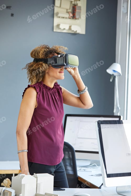 Preview: Female architect looking through virtual reality headset at office desk