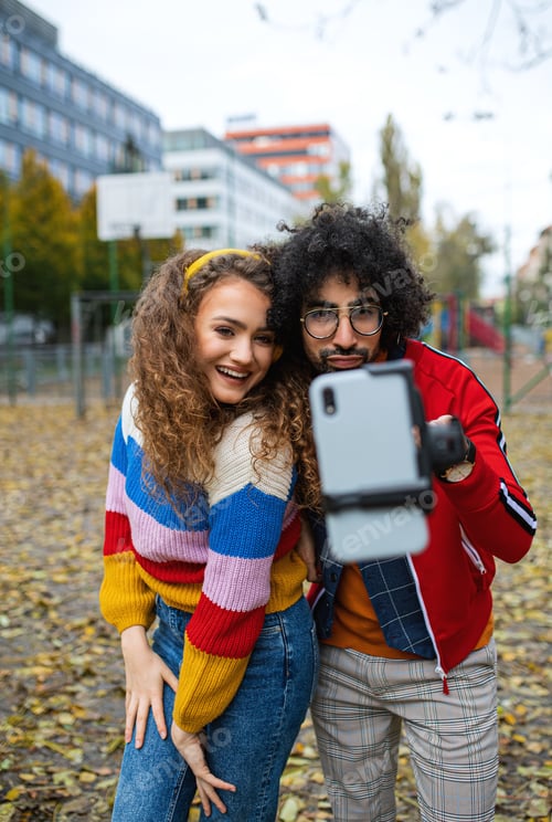 Preview: Young couple with smartphone making video for social media outdoors in park.