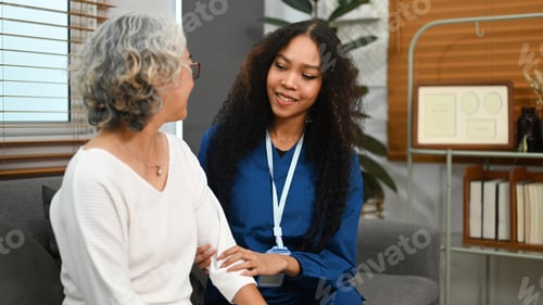 Preview: Elderly woman talking with caring young nurse, receiving home care physical and moral support.