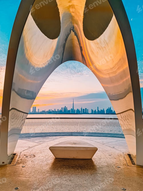 Preview: Vertical shot of an Arch above a bench near the body of water in Dubai Creek Harbor