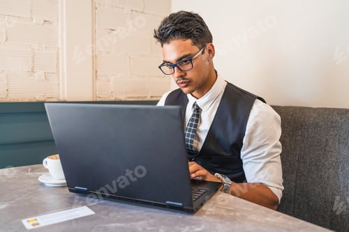 Preview: Young Man Works on Laptop in Urban Cafe