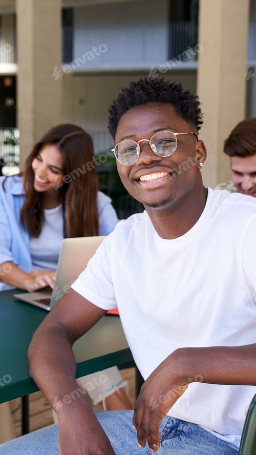 Preview: African American student smiles sincerely while sitting in college study hall with his classmates