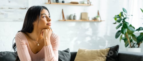 Preview: panoramic shot of pensive african american woman sitting on sofa and looking away