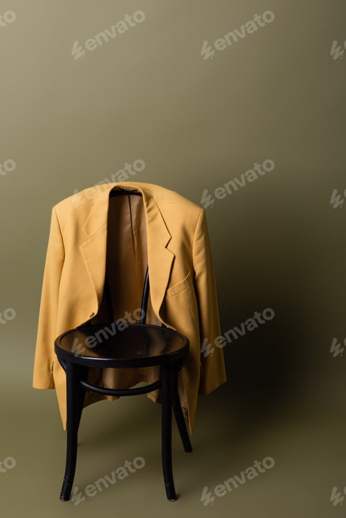 Preview: fashionable yellow blazer hanging on black wooden chair on olive green background