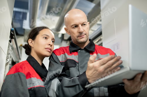 Preview: Serious bald mature foreman in workwear holding laptop and pointing at data