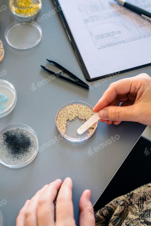 Preview: Female scientist hands taking sample of small plastic particles from glitter on petri dish in lab