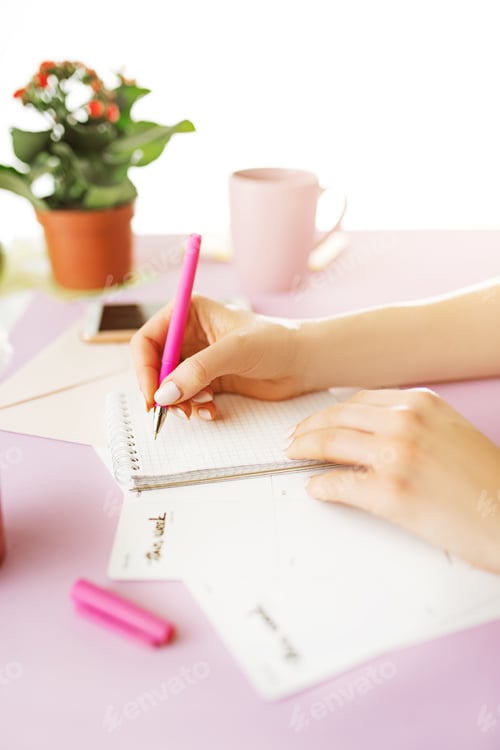 Preview: The female hands holding pen. The phone on trendy pink desk.