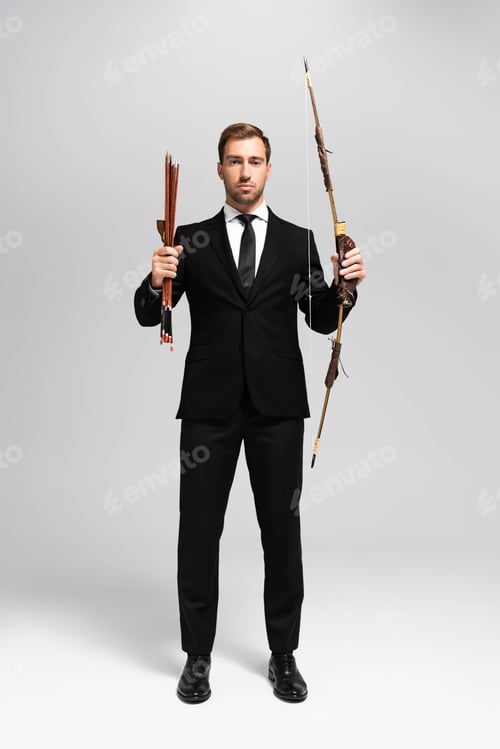 Preview: handsome businessman in suit holding bow and arrows on grey background