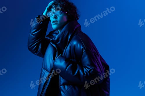 Preview: Man in winter down jacket model posing with glasses, hipster lifestyle, portrait blue background