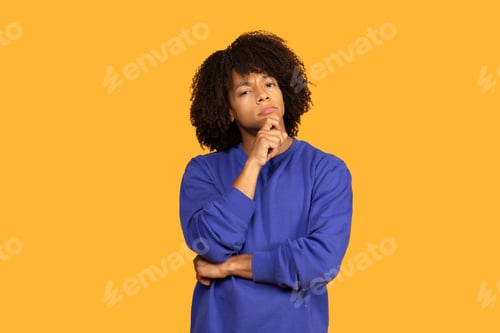 Preview: Young Man With Curly Hair Thinking on a Yellow Background