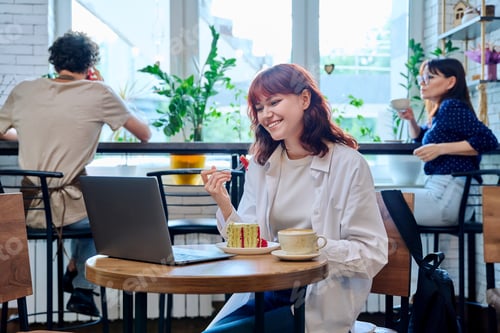 Preview: Female college student with laptop in cafe, with cup of coffee, piece of cake