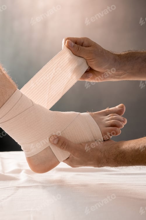 Preview: Hands of clinician holding foot of male patient while wrapping it with bandage