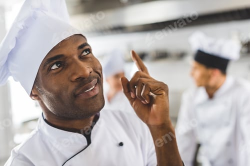 Preview: handsome african american chef pointing up at restaurant kitchen