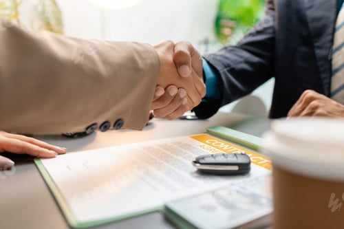 Preview: A car sales representative and a customer shake hands after signing a vehicle purchase contract.