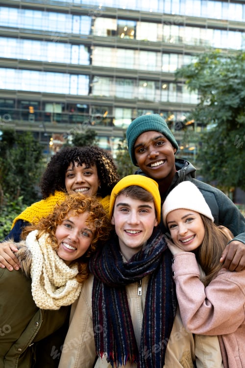 Preview: Vertical portrait of happy multiracial friends looking at camera during winter time in the city.