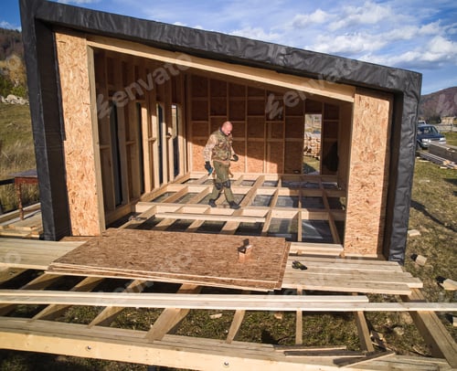 Preview: Male builder working with screwdriver inside of future wooden frame house.