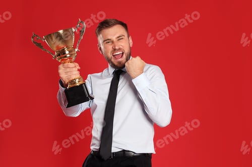 Preview: Portrait of happy young businessman with gold trophy cup on red background