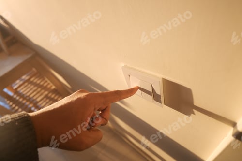 Preview: Hand pressing light switch on wall in a bright room at sunset