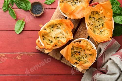 Preview: Filo pies with soft feta cheese and spinach in ceramic molds on old red wooden table backgrounds. Fi