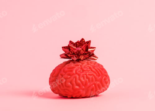 Preview: Human brain model with red festive bow on pastel pink background.