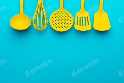 Preview: Yellow Plastic Kitchen Utensils Over Turquoise Blue Background With Copy Space