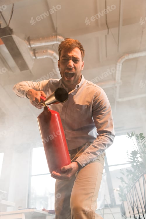 Preview: handsome businessman holding extinguisher and screaming in office with smoke