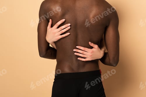 Preview: Back cropped view of sexy interracial couple hugging on beige