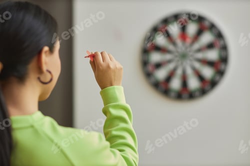 Preview: Back view closeup of young woman playing darts and aiming shot