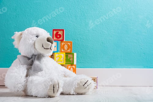Preview: White teddy bear sitting on floor with colorful numbered blocks in playroom