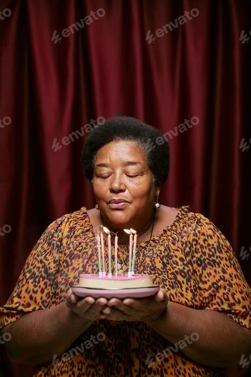 Visualização: Retrato de mulher negra de meia idade soprando velas no bolo de aniversário