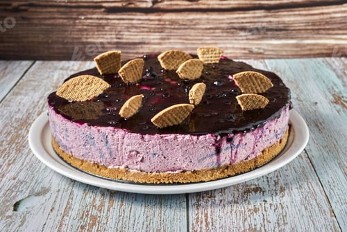 Preview: Forest fruit mousse cake decorated with pieces of biscuit, on a wooden background.
