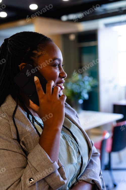 Preview: Profile of happy plus size african american casual businesswoman talking on smartphone in office