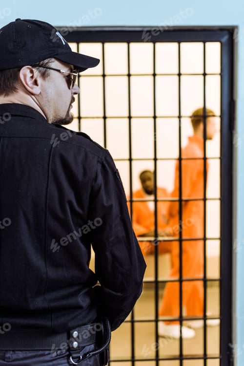 Preview: rear view of prison officer standing near prison cell with multicultural inmates