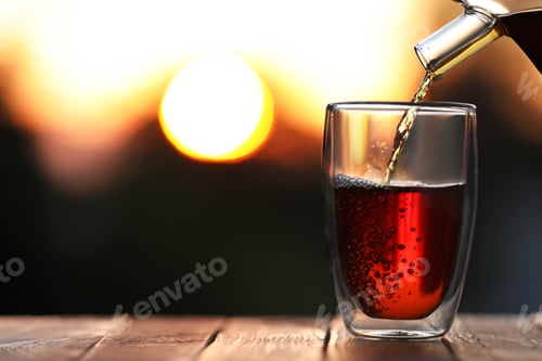 Preview: Pouring delicious tea into glass on wooden table against blurred background, closeup. Space for text