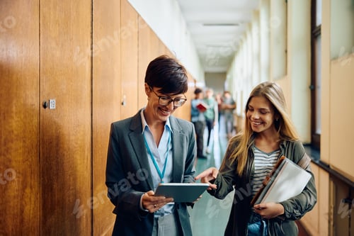 Preview: Happy high school teacher and her student using touchpad in a hallway.