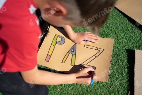 Preview: Young activist drawing peace sign in spanish on cardboard: promoting peace