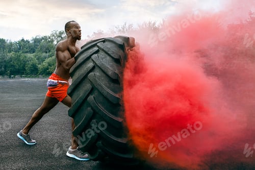 Preview: Handsome muscular man flipping big tire outdoor.