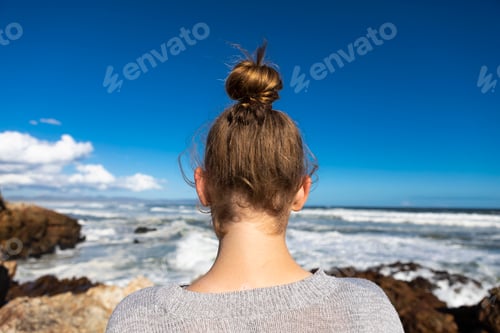 Preview: Teenage girl looking down onto the rocks on the coastline, surf waves breaking