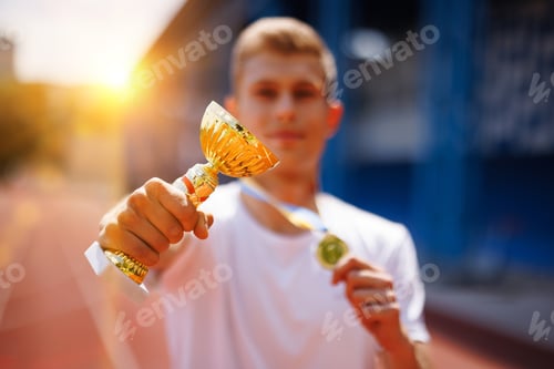 Preview: Young athlete with gold trophy and medal on running track