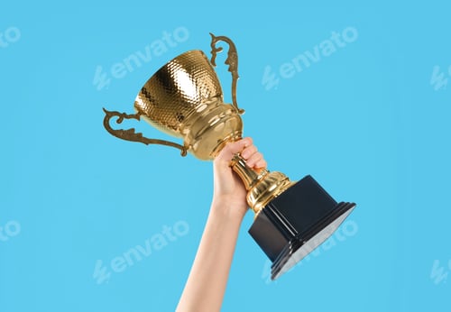 Preview: Woman holding gold trophy cup on light blue background, closeup