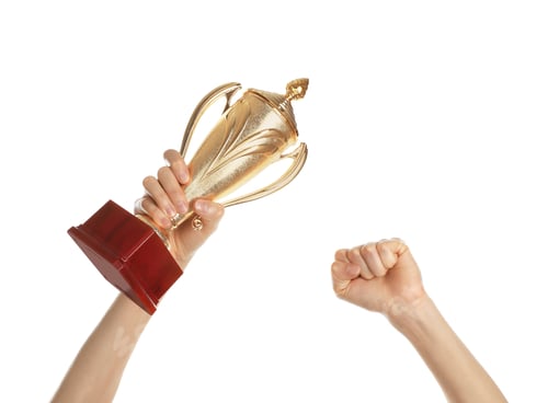 Preview: Young woman holding gold trophy cup on white background, closeup