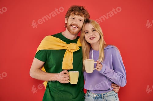 Preview: positive young couple holding cups of coffee on coral background, morning routine, vibrant colors,