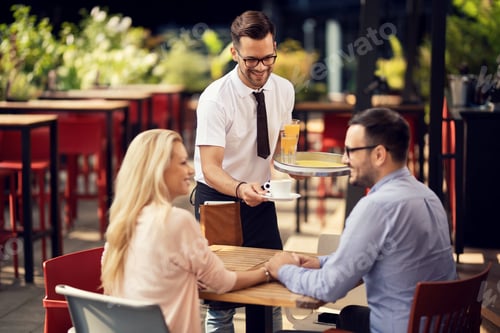 Preview: Young happy waiter serving coffee to a couple in a cafe.