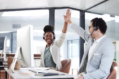 Preview: Shot of two call centre agents giving each other a high five while working in an office